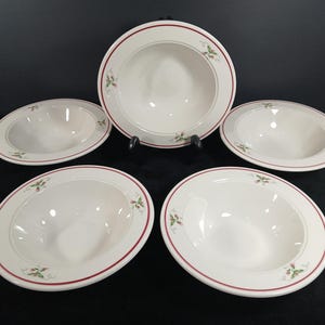 May include: A set of five white ceramic bowls with a red border and a delicate floral design. The bowls are oval-shaped and appear to be for serving soup or pasta. The bowls are arranged on a black surface.
