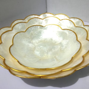 Puede incluir: Juego de tres cuencos decorativos con diseño de borde festoneado. Los cuencos son blancos con acabado nacarado y ribete dorado. Ideales para servir aperitivos o exhibir objetos decorativos.