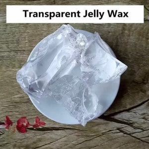 May include: A clear, transparent jelly wax in a white dish. The wax is in a solid form and has a smooth, glassy texture.