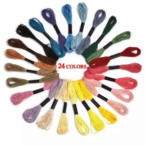 Puede incluir: Un conjunto de 24 carretes de hilo de bordar en una variedad de colores, dispuestos en un c&iacute;rculo. Los carretes est&aacute;n envueltos en hilo negro y tienen un fondo blanco.