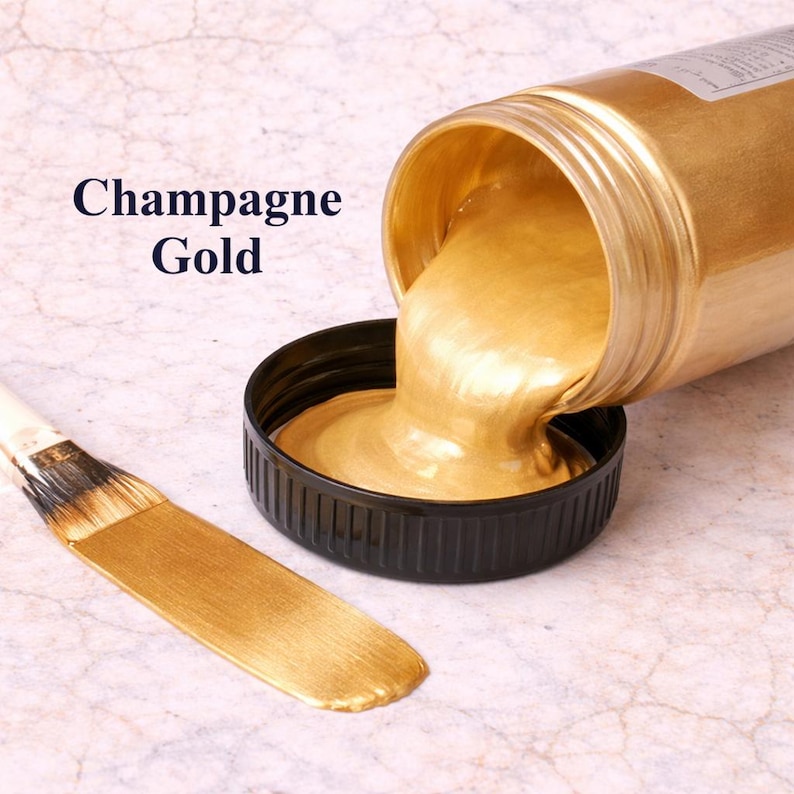 Champagne gold metallic acrylic paint pouring from a jar into a lid with a matching champagne gold brushstroke, shown in a square product image on a soft marble background.
