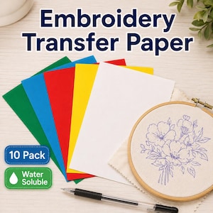 May include: A 10-pack of water-soluble embroidery transfer paper in green, blue, red, yellow, and white sheets. The set includes a wooden embroidery hoop containing fabric with a blue floral line drawing and a black ink pen for tracing designs.