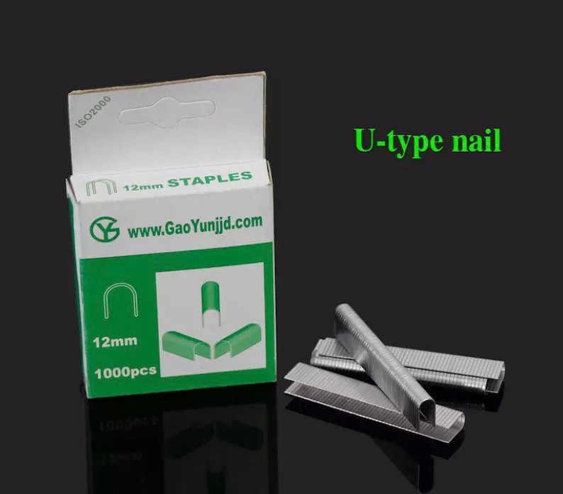 May include: A box of 12mm staples, containing 1000 pieces, with the text "U-type nail". The box is white and green, with the website address www.GaoYunjd.com. Several silver staples are scattered around the box.