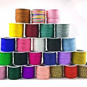 May include: A collection of spools of colourful waxed cord, arranged in a pyramid shape. The cords are in various colours, including red, blue, green, yellow, purple, pink, brown, and white.
