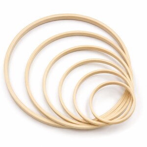 May include: A set of five nested circular embroidery hoops made of light-colored wood. The hoops are arranged in a gradient of sizes from largest to smallest, each featuring a smooth, rounded frame designed for holding fabric taut during needlework.