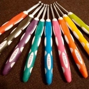 May include: A set of nine crochet hooks arranged in a fan pattern, each featuring a metallic hook and a colorful ergonomic handle with white oval accents. The handles are labeled with sizes ranging from 2.0mm to 6.0mm in various bright colors.