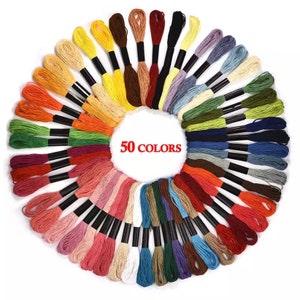 Puede incluir: Un conjunto de 50 carretes de hilo de bordar en una variedad de colores, dispuestos en un c&iacute;rculo. Los carretes son todos del mismo tama&ntilde;o y tienen bobinas de pl&aacute;stico negro. El texto "50 COLORS" est&aacute; impreso en rojo en el centro del c&iacute;rculo.
