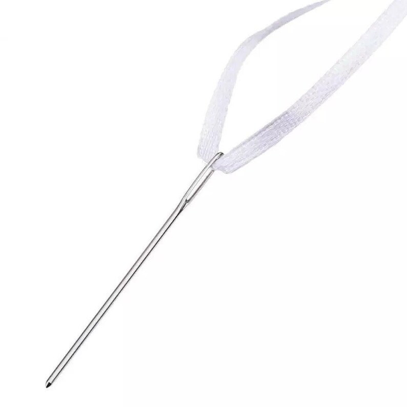 May include: A close-up of a silver needle threaded with a white ribbon.