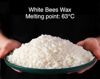 Puede incluir: Un bol blanco lleno de copos de cera de abejas blanca. El texto "White Bees Wax Melting point: 63°C" está escrito encima del bol.