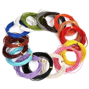 Puede incluir: Una colección de 18 carretes de cordón de cuero de colores, cada uno envuelto en un círculo. Los cordones están dispuestos en un círculo, con los colores alternando alrededor del círculo. Los cordones son todos del mismo tamaño y grosor.