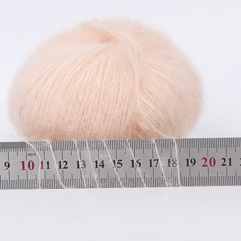 May include: A ball of pale pink yarn measured against a ruler. The yarn is 10 cm wide.