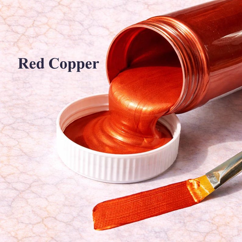 Red copper metallic acrylic paint pouring from a jar into a lid with a matching red copper brushstroke, shown in a square product image on a soft marble background.