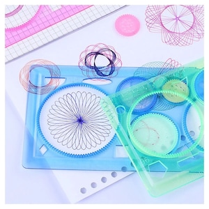 May include: A set of blue and green plastic drawing stencils for creating geometric patterns. The stencils feature various shapes, including circles, squares, and triangles.