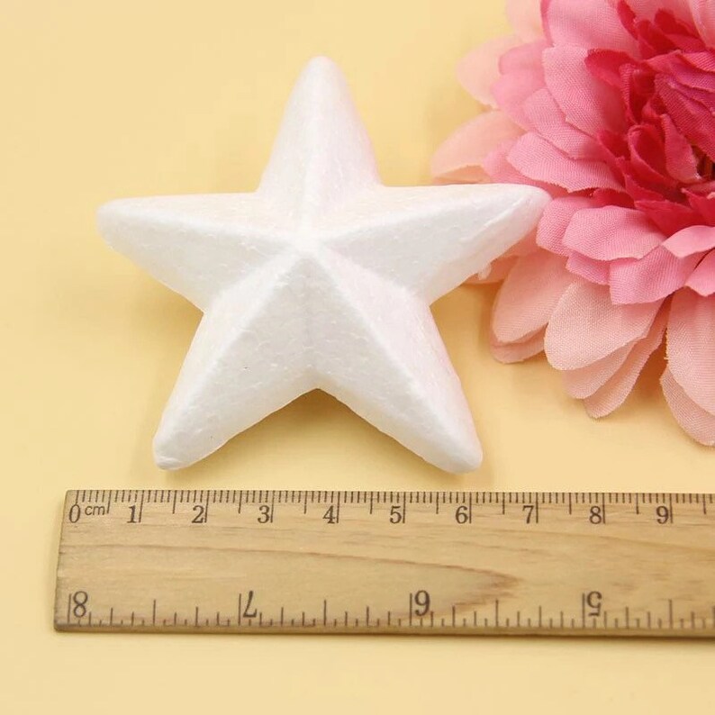 May include: A white foam star measuring 6 inches across. The star is sitting on a light brown surface next to a ruler.