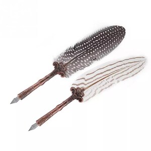 Pode incluir: Duas canetas de pena de estilo antigo com pontas de metal ornamentadas e penas de pena. Uma pena &eacute; preta e branca salpicada, a outra &eacute; branca com listras pretas.