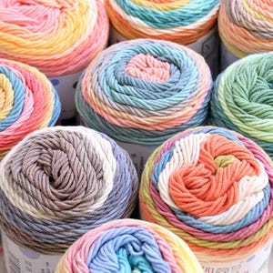 May include: A collection of multiple yarn skeins featuring variegated color patterns. Each skein consists of twisted strands in various pastel and vibrant hues, including pink, orange, yellow, blue, green, and grey, arranged in circular, layered formations.