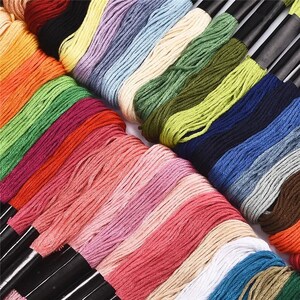 Puede incluir: Una colecci&oacute;n de carretes de hilo de bordar en una variedad de colores, incluyendo rojo, verde, azul y amarillo. Los carretes est&aacute;n dispuestos en filas y est&aacute;n ordenados cuidadosamente.