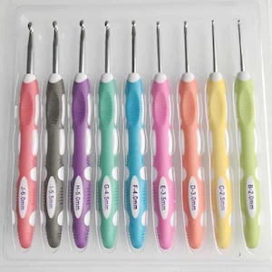 May include: A set of nine crochet hooks in a clear plastic tray, each with a colored rubber handle and a metal hook. The handles are labeled with letters and sizes ranging from B-2.0mm to J-6.0mm, featuring pink, gray, purple, green, blue, and yellow.