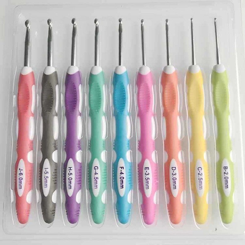 May include: A set of nine crochet hooks in a clear plastic tray, each with a colored rubber handle and a metal hook. The handles are labeled with letters and sizes ranging from B-2.0mm to J-6.0mm, featuring pink, gray, purple, green, blue, and yellow.