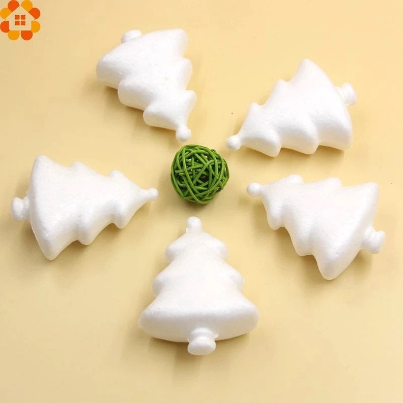 May include: Five white foam Christmas tree shapes on a light beige surface. A green woven ball is in the center of the arrangement.