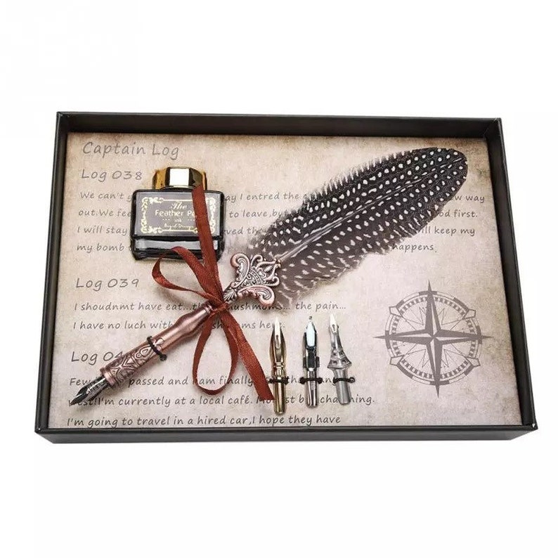 Pode incluir: Um conjunto de caligrafia numa caixa preta com uma pena de pena castanha, um frasco de tinta e cinco pontas. A caixa tem um design vintage com o texto "Captain Log" e "Log 038" na frente.