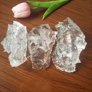 May include: Three pieces of clear, translucent, irregularly shaped gelatinous material on a brown wooden surface.