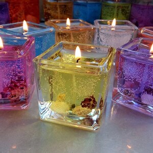 Puede incluir: Surtido de velas de gel cuadradas de vidrio en varios colores, incluyendo morado, rosa, amarillo y blanco. Cada vela tiene una peque&ntilde;a mecha y est&aacute; llena de gel transparente y elementos decorativos.