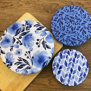 May include: Three blue and white patterned fabric covers for bowls or jars. The covers feature different designs, including floral, geometric, and a pattern of small leaves.