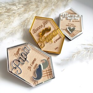 May include: Three wooden plaques with gold and silver accents. The plaques feature the word "Papa" in different styles and include the text "Bonne f&ecirc;te d'amour Jules", "Super Papa Je t'aime ROBIN", and "Melte du monde On t'aime ARES & LOUNA".