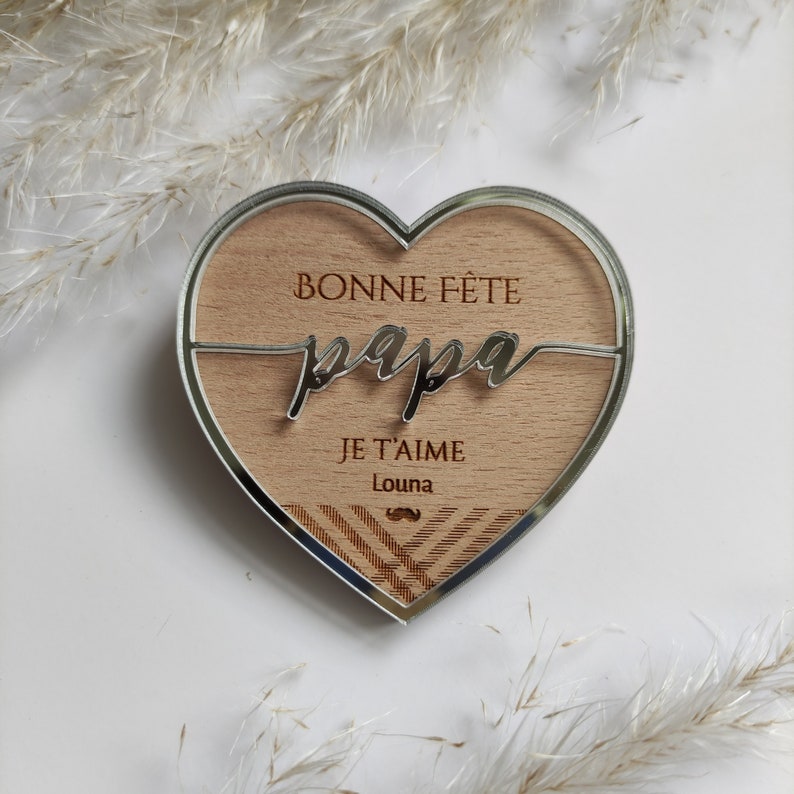 Puede incluir: Una placa de madera en forma de coraz&oacute;n con un acabado de espejo plateado. La placa tiene el texto "Bonne F&ecirc;te Papa" y "Je t'aime Louna" con un gr&aacute;fico de bigote plateado.