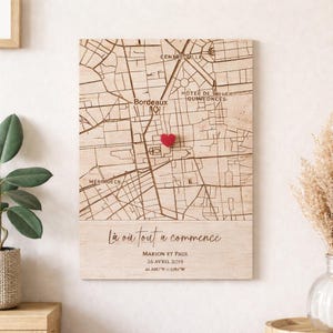 Puede incluir: Mapa de madera de Burdeos, Francia, con un corazón rojo que marca una ubicación. El mapa está grabado con nombres de calles y el texto "Là où tout a commencé", junto con nombres, una fecha y coordenadas. Una pieza decorativa.