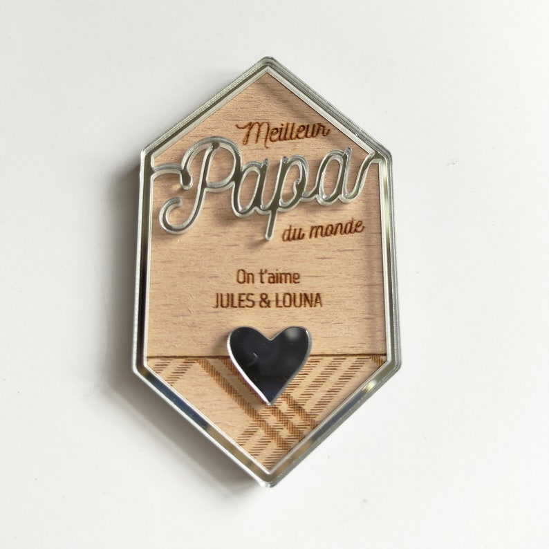May include: A wooden plaque with a silver border and a heart-shaped cutout. The plaque reads "Meilleur Papa du monde" and "On t'aime JULES & LOUNA".