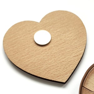 Puede incluir: Un adorno de madera en forma de coraz&oacute;n con un im&aacute;n redondo blanco pegado en la parte delantera.