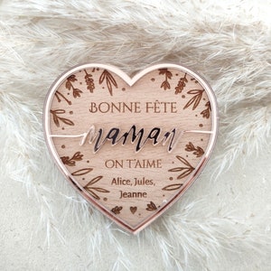 Puede incluir: Una placa de madera en forma de coraz&oacute;n con un borde de oro rosa. La placa tiene un dise&ntilde;o floral y el texto "Bonne F&ecirc;te Maman On T'aime Alice, Jules, Jeanne".