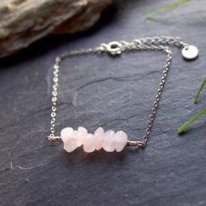 Op de afbeelding: Een delicate zilveren kettingarmband met een cluster van lichtroze rozenkwartsstenen.
