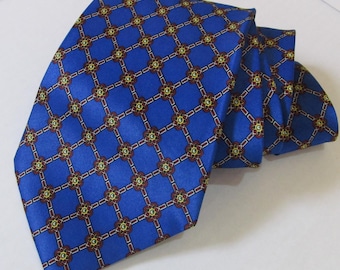 Puede incluir: Una corbata de color azul brillante con un patrón geométrico repetitivo. El diseño consiste en líneas entrelazadas de color rojo oscuro y blanco que forman rombos, con pequeños motivos florales estilizados en rojo, amarillo y verde.