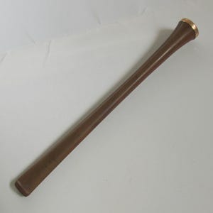 Puede incluir: Un bate de béisbol de madera marrón con un anillo dorado en la parte superior. El bate es cónico y tiene un acabado liso. El bate está en ángulo diagonalmente en el marco.