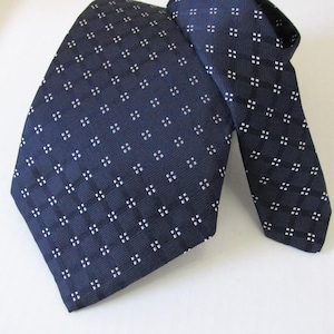 May include: A dark navy blue necktie featuring a repeating grid pattern of small white squares. The fabric has a subtle ribbed texture, and the design consists of intersecting lines forming a series of evenly spaced squares across the entire surface.