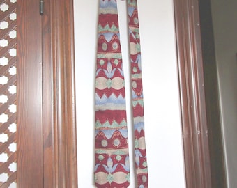 Puede incluir: Una corbata con un patrón repetitivo de formas geométricas en rojo oscuro, azul claro y beige. El diseño incluye motivos florales estilizados, elementos circulares y líneas dentadas dispuestas en bandas horizontales sobre la tela.