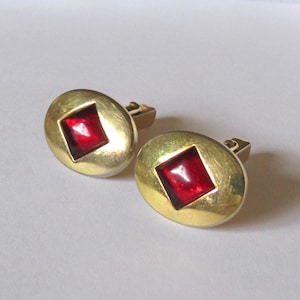 May include: Two gold-coloured cufflinks, each featuring a red, square-cut stone set within an oval frame. These classic cufflinks are designed for formal occasions. The red stone provides a striking contrast.