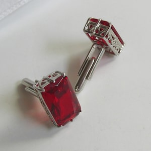 Peut inclure: Une paire de boutons de manchette rectangulaires avec de grandes pierres facettées rouge foncé, serties dans des montures en métal argenté dotées d'un treillis ajouré complexe sur les côtés et de fermoirs à bascule articulés.