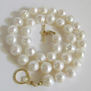 Può includere: Una collana composta da grandi perle bianco-avorio e lucenti. Le perle sono infilate insieme, formando una forma circolare. La collana presenta una chiusura color oro con un design a forma di cuore. Le perle hanno un diametro di circa 1,3 cm.