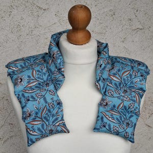 Könnte beinhalten: Ein hellblaues Nackenband mit einem Blumenmuster in Weiß, Braun und Marineblau. Das Band wird auf einer weißen Schaufensterpuppe präsentiert und hat einen Holzknopf oben.