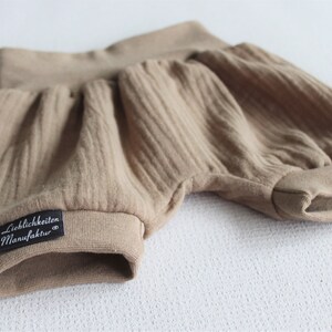 May include: A pair of brown cotton baby bloomers with a black label that reads "Lieblichkeiten Manufaktur".