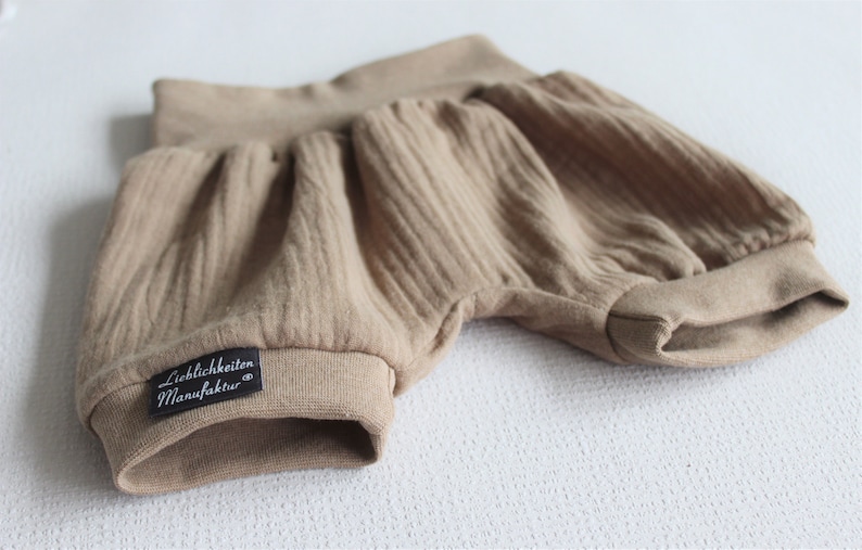 May include: A pair of brown cotton baby bloomers with a black label that reads "Lieblichkeiten Manufaktur".