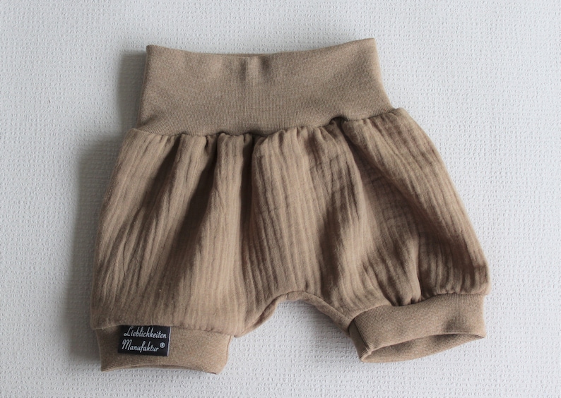 May include: Brown baby bloomers with a ribbed texture and a black label that says "Lieblichkeiten Manufaktur".