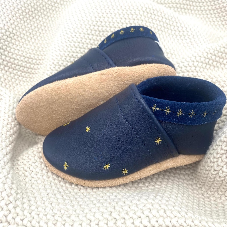 Die Kinderschuhe mit Sternstickerei sind perfekt für kleine Sternenfans. Mit liebevoll gestalteten, funkelnden Sternen verziert, bieten diese Schuhe nicht nur Komfort, sondern auch einen Hauch von Magie. Hier in Blau mit Gold bestickt.