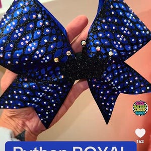 May include: A large, royal blue cheerleading bow with a black center. The bow is decorated with small, sparkling rhinestones and has a pattern resembling snake scales. The text "Python ROYAL" is displayed on a blue banner.