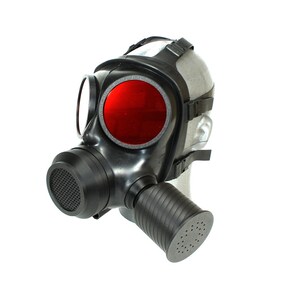 Könnte beinhalten: Eine schwarze Gasmaske mit einer markanten runden roten Linse, einem vorderseitigen runden Filtergehäuse mit Netzgitter und einem seitlich angebrachten zylindrischen Filteraufsatz, befestigt durch verstellbare schwarze Gummibänder am Kopf.