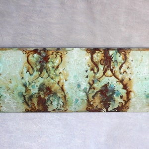 Könnte beinhalten: Eine dekorative Wandplakette aus Metall mit einer geschwungenen Form und einem verwitterten, vintage-inspirierten Design. Die Plakette zeigt ein sich wiederholendes Muster aus verzierten Wirbeln und floralen Motiven in Braun-, Grün- und Weißtönen.